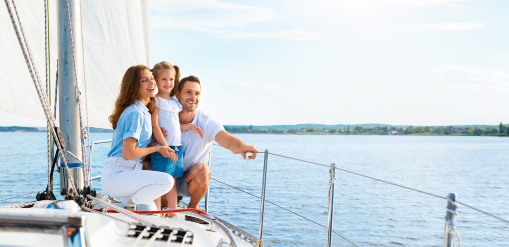 Parents And Daughter Sitting On Yacht Deck Sailing Across Sea Enjoying Summer Vacation Outside.